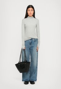 Maglietta grigia a maniche lunghe con colletto alto, jeans a gamba larga azzurri chiari e borsa a tracolla nera con trama. Colori solidi in tutto.