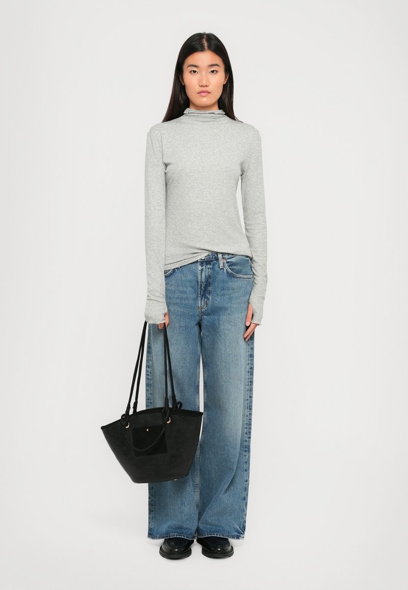 Maglietta grigia a maniche lunghe con colletto alto, jeans a gamba larga azzurri chiari e borsa a tracolla nera con trama. Colori solidi in tutto.