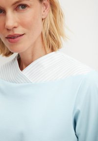 Lichtblauw shirt met een witte kraag met blauwe strepen. Zachte stof, lichtgewicht ontwerp, met een ronde halslijn en een lichte draping.