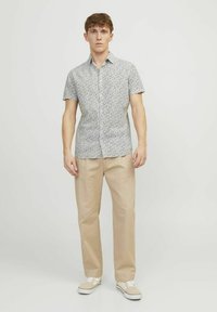 Maglietta a maniche corte bianca con motivo floreale blu, abbinata a pantaloni beige e sneakers chiare. Realizzata in misto cotone, design comodo e rilassato.
