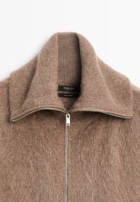 Maglione in cashmere marrone con colletto alto, chiusura a zip e texture a costine. Presenta l'etichetta del marchio all'interno del colletto.