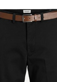 Pantaloni neri con una cintura in pelle marrone dotata di una fibbia argentata. Il tessuto ha una consistenza liscia. L'etichetta riporta "JACK & JONES".