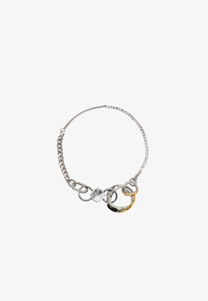 Srebrna bransoletka łańcuszkowa z połączonymi pierścieniami, akcentem w postaci przezroczystego kamienia oraz złoconym ogniwem. Gładkie i wypolerowane tekstury.