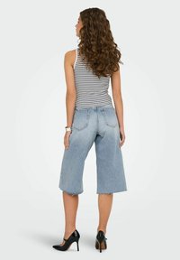 Culotte in denim blu chiaro con orlo sfilacciato, abbinati a una canotta a righe grigie e bianche e tacchi alti neri.