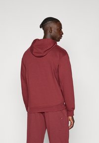 Bordeauxfarbener Pullover mit Kapuze, Kängurutasche, gerippten Bündchen und verstellbarem Kordelzug in der Kapuze. Weicher Stoff, schlichtes Design und keine sichtbaren Logos oder Muster.