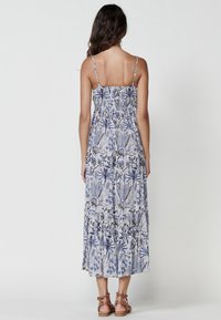 Rochie maxi cu un model floral albastru și alb, bretele ajustabile, bust plisat și margine cu volane în straturi. Sandale maronii cu bretele.