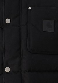 Schwarze Puffy-Jacke mit gestepptem Design, ausgestattet mit silbernen Druckknöpfen und einer linken Brusttasche mit einem schwarzen quadratischen Logo-Patch.