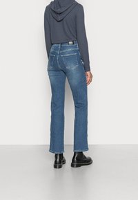 High-waisted blue denim jeans with a slim fit, featuring a classic five-pocket design and subtle fading, paired with a dark hoodie and black boots.