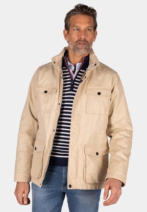 Beige jas met een hoge kraag, vier externe zakken en drukknoopsluitingen. Gemaakt om te dragen over een marineblauw gestreefd truitje. Gladde textuur.