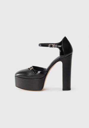 Black platform shoes with a rounded toe, ankle strap, and silver buckle detail. Made of smooth patent leather; features a thick block heel.