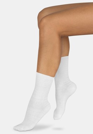 Weiße Baumwollknöchelsocken mit geripptem Struktur, glatter Oberfläche und einem stabilen Bündchen, positioniert auf nackten Beinen.