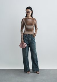 Brown and white striped long-sleeve top, loose blue jeans, pink clutch bag, with wide-leg design and slight texture. Accessories include glasses.