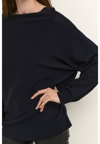 Navy sweater in a soft knit material with a loose design, featuring a wide neckline and ribbed cuffs and hem. Smooth texture with dropped shoulders.