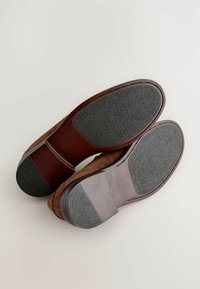 Zapatos de ante marrón con suelas de goma, que cuentan con un agarre texturizado negro y suaves acentos marrones en el talón y los laterales.
