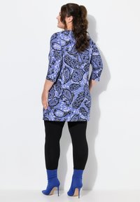Modrá tunika s vzorem paisley a černými akcenty, s třičtvrtinovými rukávy, v kombinaci s černými legínami a modrými vysokými kotníkovými botami.