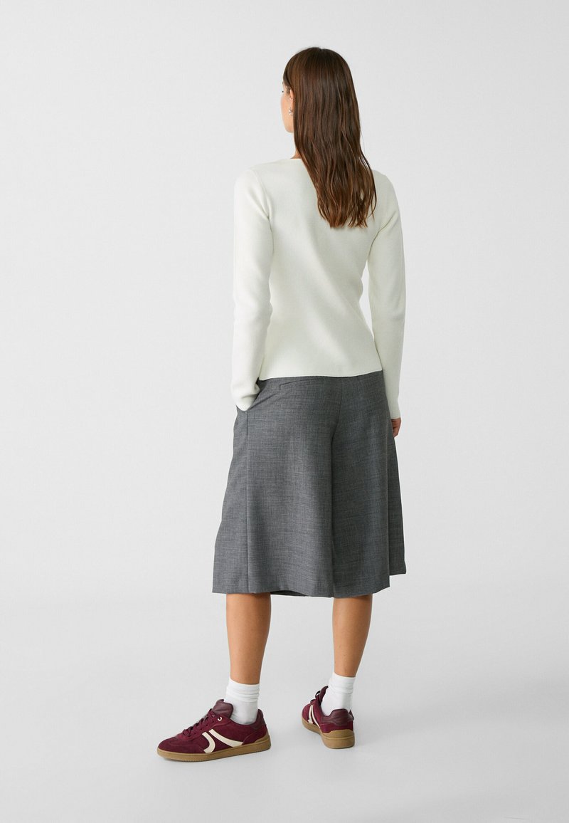 Maglietta bianca a maniche lunghe abbinata a una gonna plissettata grigia e sneakers borgogna. L'outfit presenta una texture liscia e un design semplice.