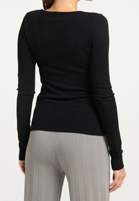 Top nero a maniche lunghe realizzato in morbido tessuto a maglia, con scollatura rotonda e orlo a coste. Abbinato a pantaloni grigi a coste.