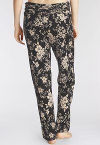 Bloemenleggings in zwart met een romige beige patroon, voorzien van een zachte, rekbare tailleband en een ontspannen pasvorm. Het materiaal lijkt lichtgewicht en soepel.