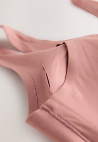 Roosa varrukateta topp, mis on valmistatud pehmest kangast, millel on kaeluse lähedal lõikekoht, puhas õmblus ja sile tekstuur.