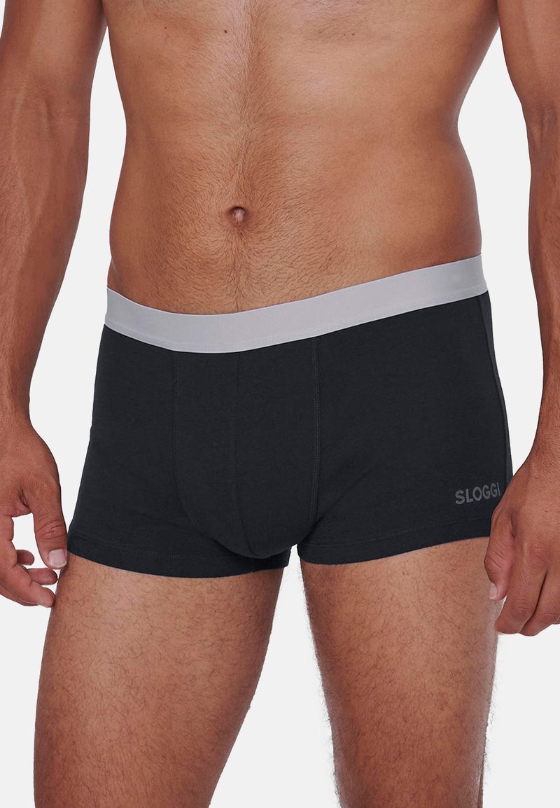 Männlicher Oberkörper, bekleidet mit schwarzen Boxer-Shorts mit grauem Bund und dem "SLOGGI"-Logo am linken Bein.