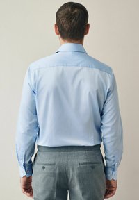 Chemise bleu clair à manches longues avec poignets à boutons, assortie à un pantalon gris cintré avec poches arrière et accents de boutons.
