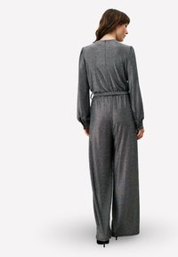 Combinaison grise pailletée à manches longues, taille cintrée et jambes larges. Texture lisse avec une fermeture éclair au dos et un éclat discret.