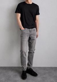 T-shirt nera a girocollo, jeans grigi chiari, design aderente, texture liscia. Sneakers nere completano l'outfit, stile minimalista.