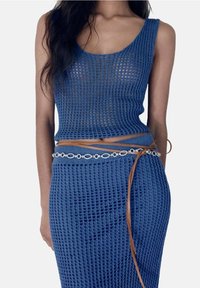 Ensemble de top sans manches et jupe tricotés en bleu, avec une texture transparente et une coupe ajustée. Accentué d'une ceinture marron et d'un détail de chaîne circulaire blanche.