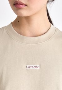 Bežna bombažna majica s krojem na okroglo in kratkimi rokavi, ki na prsih nosi belo in burgundsko rdečo oznako logotipa Calvin Klein.