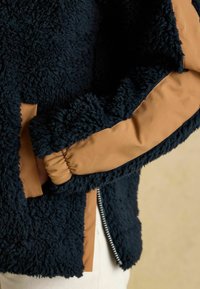 Granatowa, miękka kurtka z beżowym satynowym paskiem na rękawach. Posiada zamek błyskawiczny i teksturalny kontrast dzięki miękkiemu materiałowi.