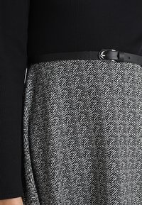 Svart ribbad topp med lång ärm, parat med en knä-lång kjol med ett svart och vitt houndstooth-mönster och ett svart bälte.