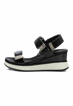 Sandalias de cuña negras con correas ajustables, acabado de charol brillante, detalles en hardware plateado y una suela blanca contrastante para mayor estabilidad.