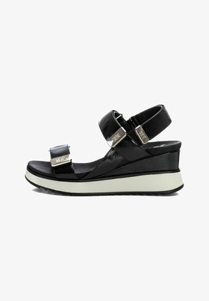 Sandalias de cuña negras con correas ajustables, acabado de charol brillante, detalles en hardware plateado y una suela blanca contrastante para mayor estabilidad.