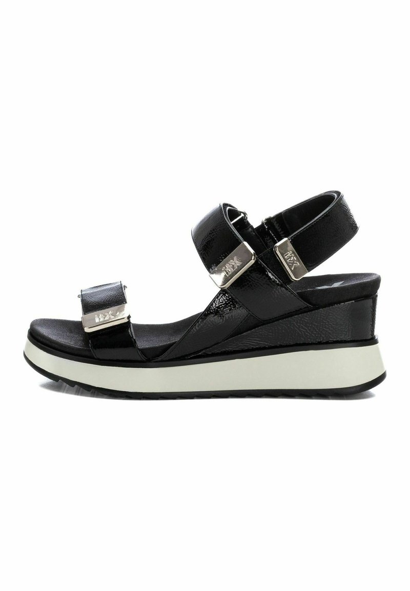 Sandalias de cuña negras con correas ajustables, acabado de charol brillante, detalles en hardware plateado y una suela blanca contrastante para mayor estabilidad.