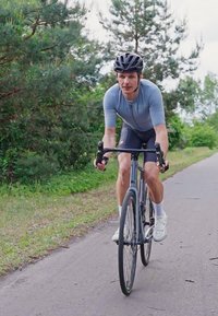 Maillot de cyclisme gris léger associé à un short noir, porté par un cycliste sur un chemin. Le vélo est équipé de pneus fins et d'un cadre élégant.