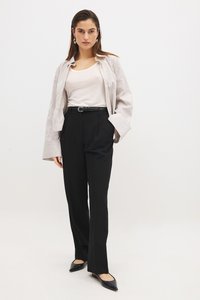Pantalones negros de corte ajustado con una pierna amplia, combinados con una blusa de manga corta beige y una camisa de raya clara y oversized. Bailarinas negras con punta.
