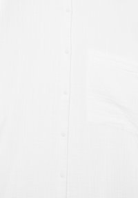 Hvid skjorte med knapper og venstre brystlomme samt subtil lodret tekstur i stoffet.