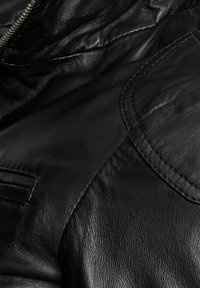 Primo piano di una giacca in pelle nera che mostra il materiale testurizzato, le cuciture, una patta della tasca e una chiusura lampo metallica parzialmente visibile.