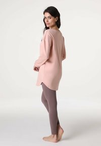 Tunica a maniche lunghe di colore rosa chiaro abbinata a leggings marroni. La tunica presenta una scollatura rotonda e un orlo leggermente curvato per una vestibilità comoda.