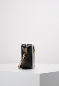 Borsa a mano in pelle nera con finitura testurizzata, tracolla in catena dorata e chiusura con zip. Forma rettangolare compatta con design minimalista.