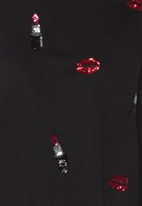 Musta kangas, jossa on punaisen ja hopean sävyisiä, kirjailtuja huulipuna- ja huuliaiheisia koristekiviä eri asetteluissa ja ko'oissa pinnalla.