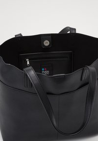 Zwarte tote bag met een gladde textuur, voorzien van twee lange handvatten, een magnetische drukknoopsluiting en een ritsvak aan de binnenkant.