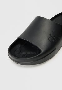 Black slide sandal with a smooth rubber upper, open toe, and textured footbed. Features an embossed logo on the side. Durable and lightweight design.