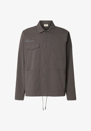 Szara lekka kurtka z kołnierzem, dwoma kieszeniami na piersi i ściągaczem u dołu. Na piersi znajduje się nadruk z logo i cyframi.