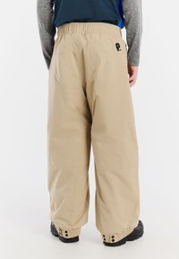 Beige waterdichte broek met elastische taille, wijde pijpen, drukknopen aan de onderkant en een achterzak met een logo. Glad, lichtgewicht stof textuur.