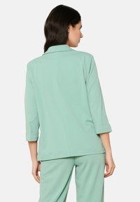 Mėtų žalios spalvos švarkas su trimis ketvirtadaliais rankovėmis, tiesaus kirpimo ir apykakle su užlenkimu. Lygus audinys su minimaliu dekoru, tinkamas įvairioms progoms.