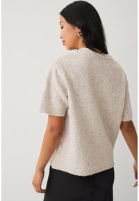 Kurzärmeliger, gestrickter Pullover in hellem Beige mit weicher Textur, Rundhalsausschnitt und leicht längerem Saum hinten. Minimalistisches Design ohne Muster.