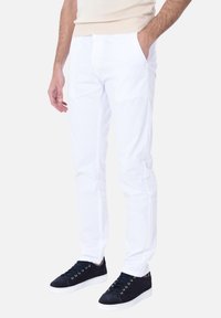Pantaloni bianchi in cotone con una vestibilità slim, dotati di tasche laterali e una superficie liscia, abbinati a sneakers in camoscio blu navy.