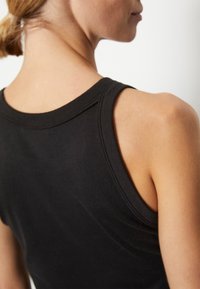Top negru fără mâneci, cu un guler rotund și o textură netedă. Prezentă cusături pe lângă brațe și pe spate.
