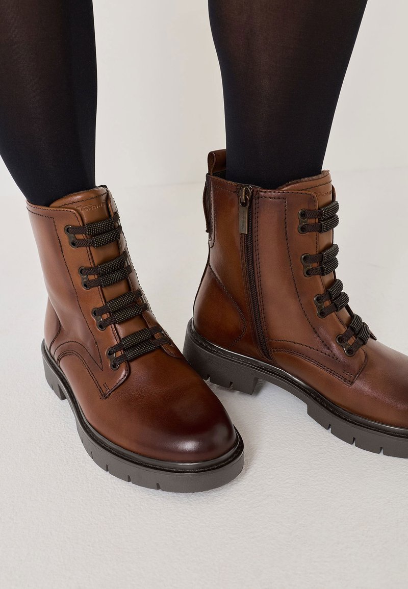 Brązowe skórzane botki za kostkę z sznurówkami i zamkiem błyskawicznym, teksturowana cholewka, okrągły nosek i masywna czarna gumowa podeszwa.